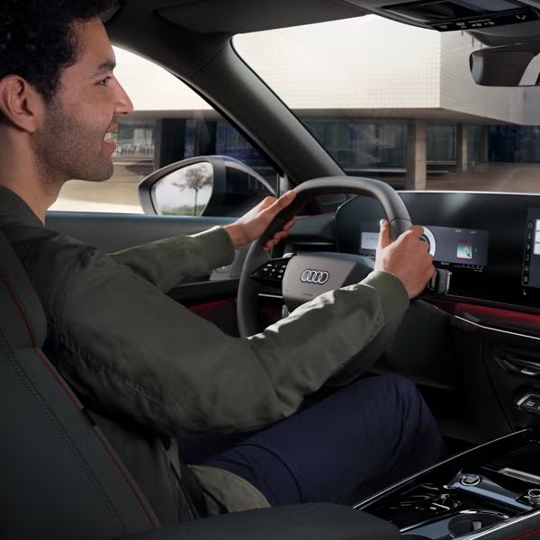 Blick von schräg hinten auf das Cockpit des Q3 Sportback, ein junger Mann sitzt am Lenkrad.