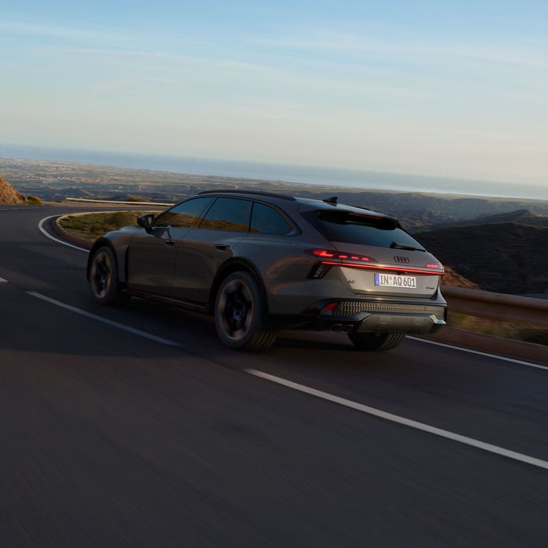 Der Audi A6 allroad schräg von hinten durchfährt eine langgezogene Kurve auf einer Landstraße.