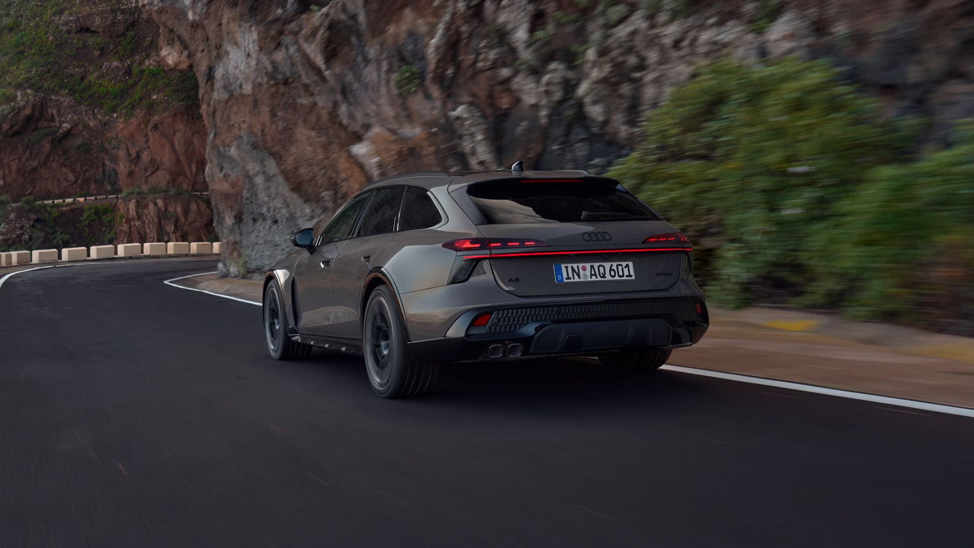 Der Audi A6 allroad schräg von hinten in voller Fahrt auf einer Gebirgsstraße. Rechts ragen steile Felswände auf.
